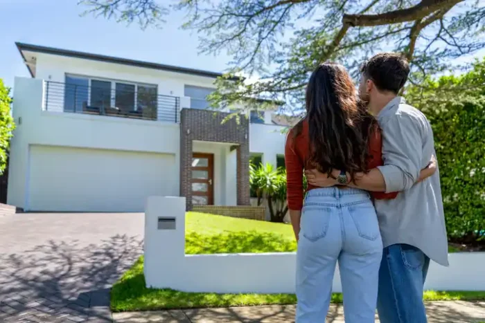 Couple arm in arm in front of their new home in Australia