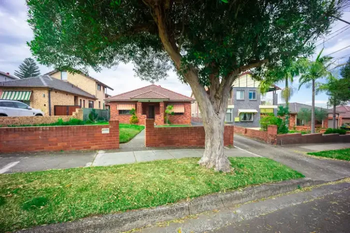 Old home seen from curb behind a big tree in Australian suburbs.